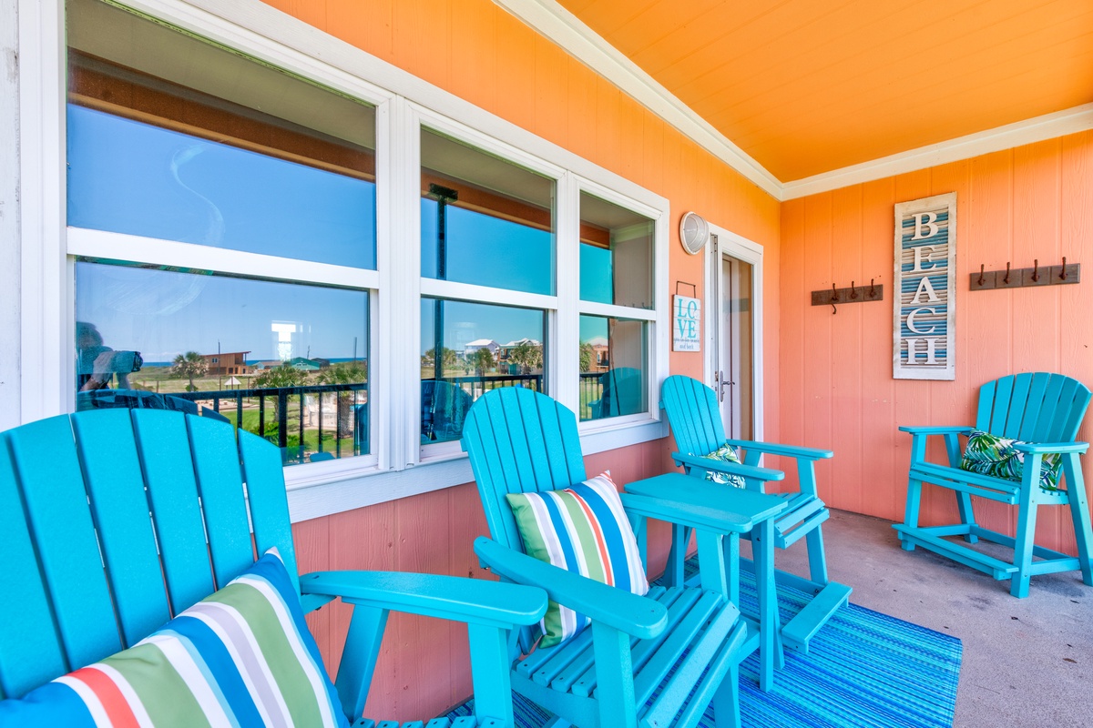 Relax in vibrant turquoise Adirondack chairs on your private covered balcony, where coral walls and cheerful coastal décor create the perfect seaside retreat.