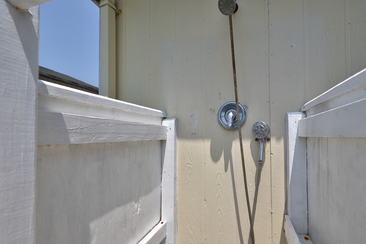 This private outdoor shower features natural light from above and a handheld showerhead, perfect for rinsing off after a day at the beach.
