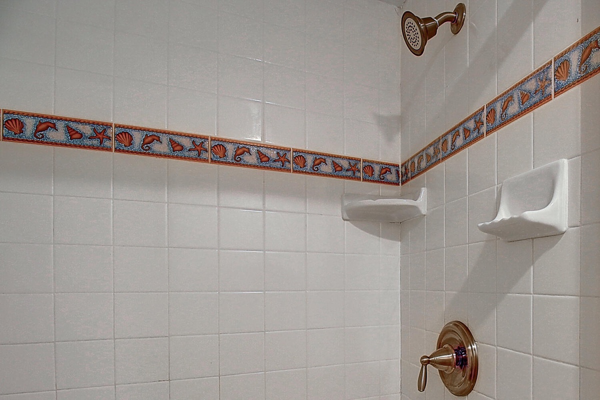 Your private shower features elegant tiled walls with decorative accents, built-in shelving for toiletries, and quality bronze fixtures.
