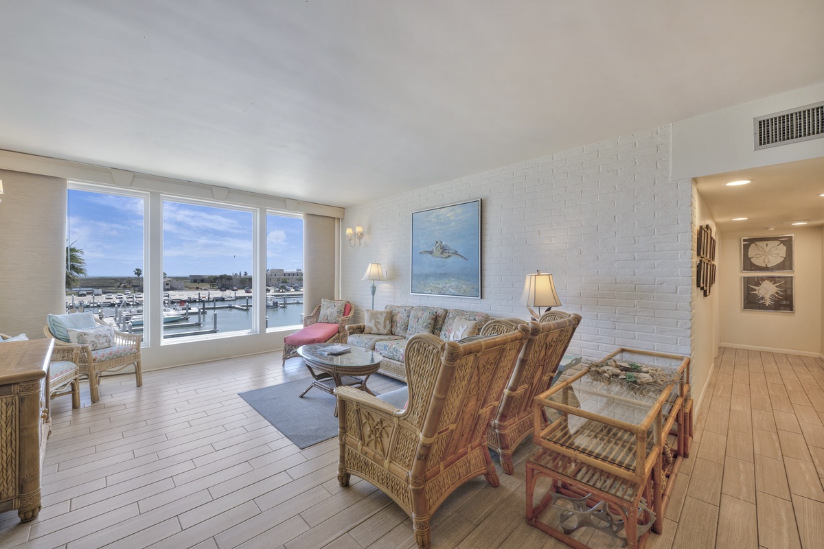 Relax in your coastal living room with wicker furnishings and panoramic marina views through floor-to-ceiling windows.