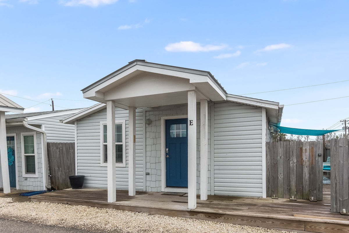Charming coastal cottage with bright blue door and covered porch offers a welcoming retreat steps from the beach.