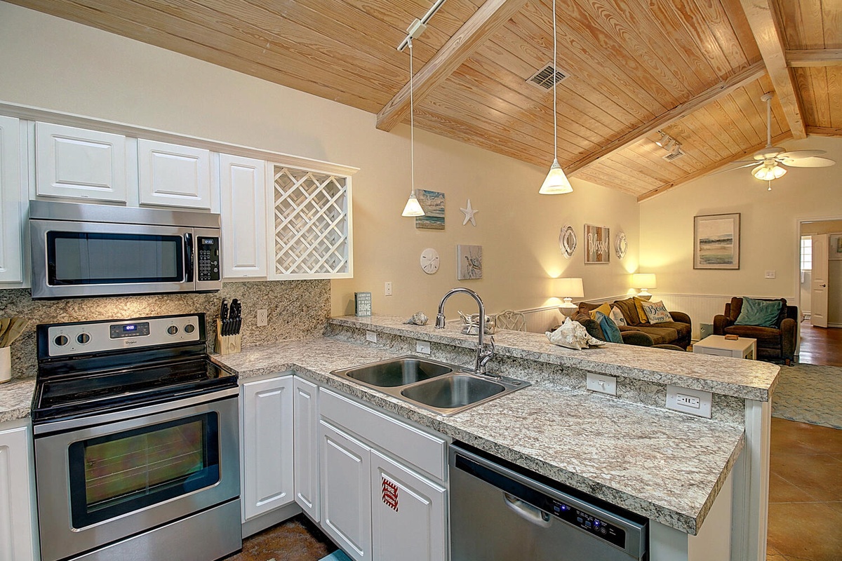 Your open-concept kitchen flows seamlessly into the living space, where granite counters and warm wood beam ceilings create an inviting atmosphere for cooking and gathering.