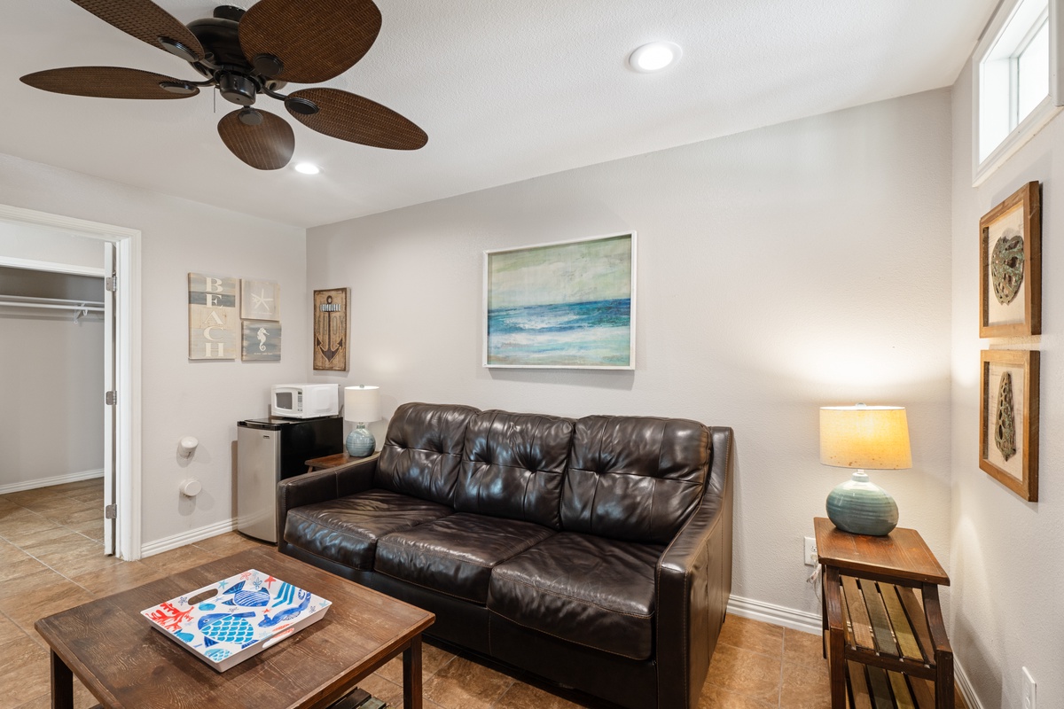 Relax in your comfortable living space featuring plush leather seating, coastal artwork, and a cooling ceiling fan for ultimate comfort.