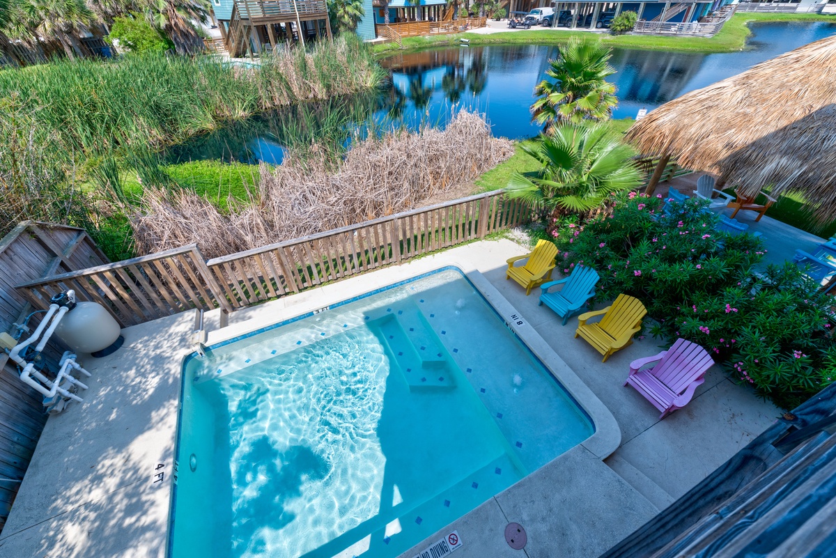 Vibrant pool area overlooks peaceful canal waters, surrounded by tropical landscaping and colorful lounge chairs in this waterfront community setting.