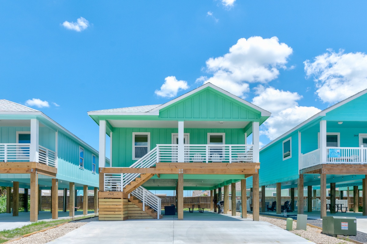Charming elevated beach cottage with vibrant green siding and covered parking beneath your coastal retreat.