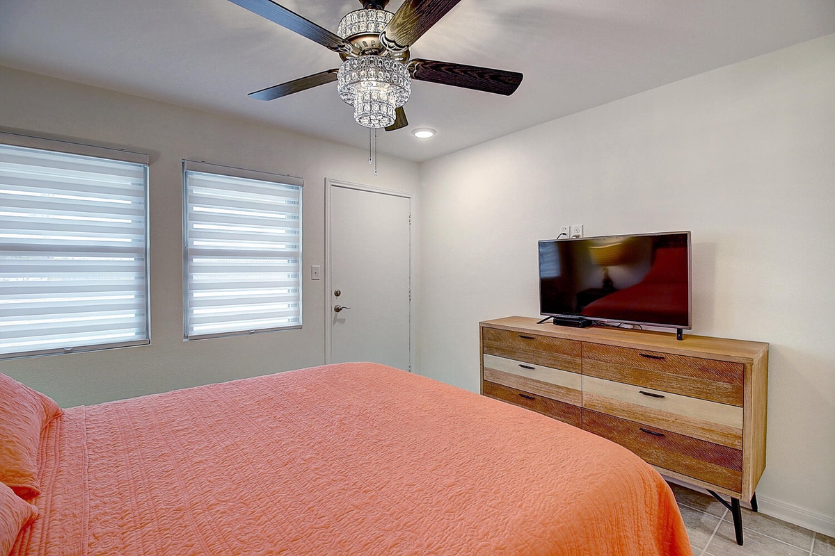Your bright bedroom features a crystal chandelier ceiling fan, stylish wood dresser, and TV for relaxing after exploring the area.