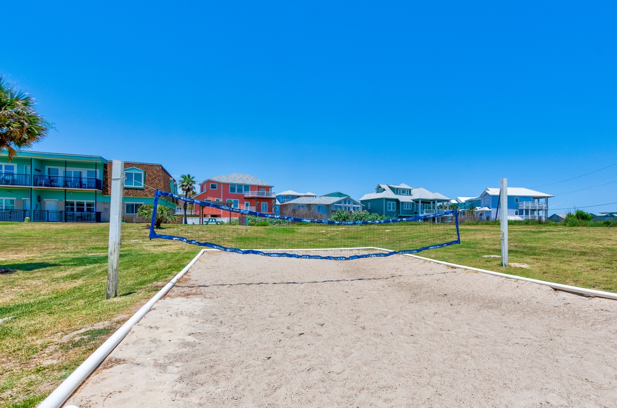 Beach volleyball court with colorful coastal rental homes nearby under brilliant blue skies.