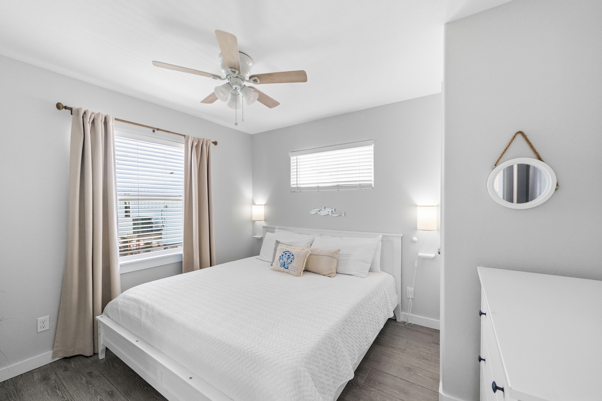 Settle into your bright, serene bedroom with its plush bed and soft coastal touches. Gentle breezes from the ceiling fan keep you cool, while natural light fills the space with calm.