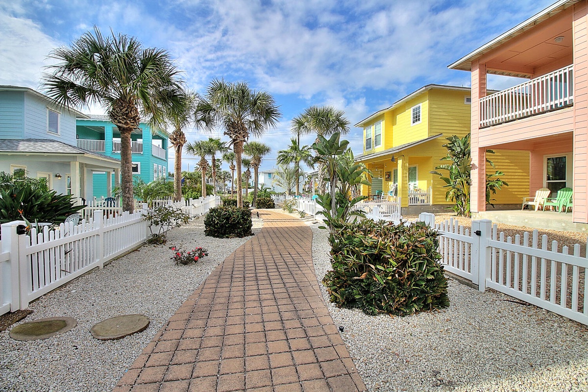 Charming tropical cottage community features colorful beachside buildings and manicured walkways lined with palm trees and native landscaping.