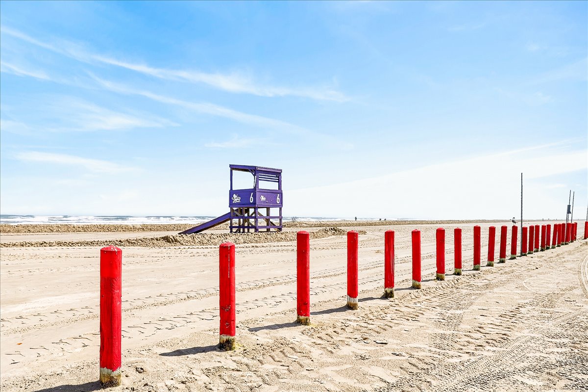 Beautiful sandy beach with lifeguard station and distinctive red posts marking the shoreline under endless blue skies.