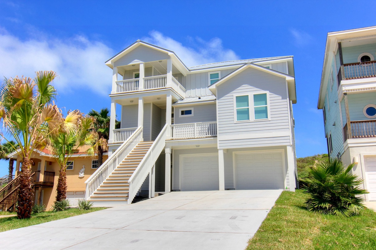 A stunning coastal home with tropical palms and bright blue skies, featuring multiple levels and balconies in a peaceful beachside neighborhood.