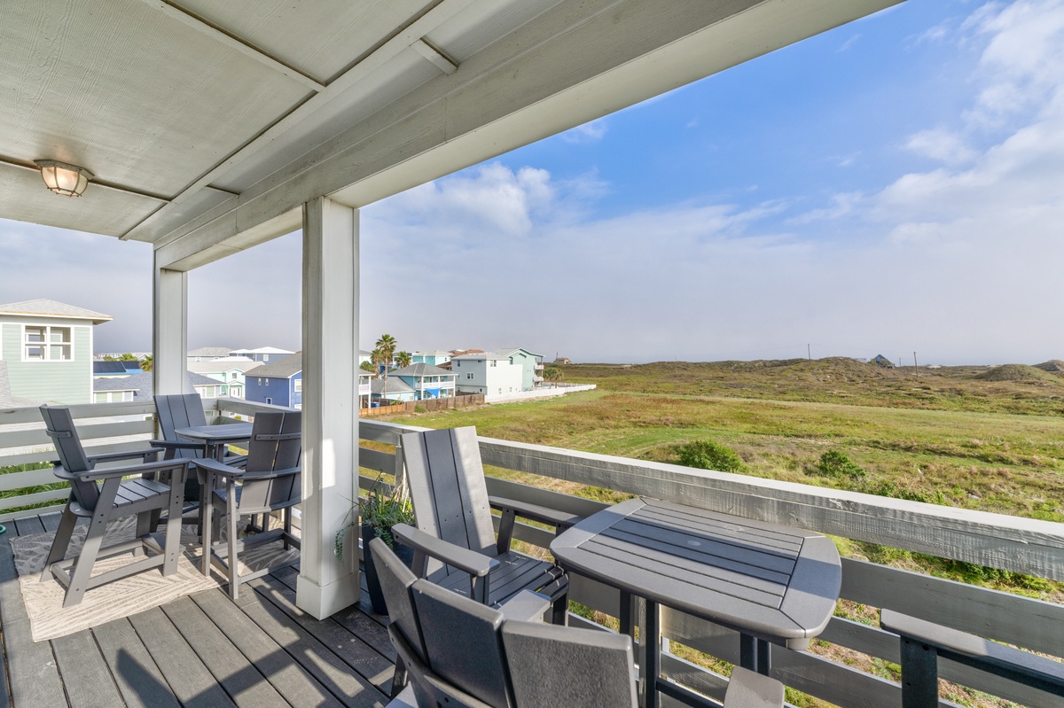 Covered balcony with comfortable seating overlooking peaceful dunes and coastal neighborhood.