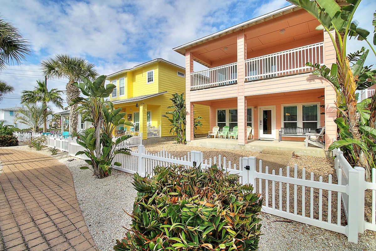 Colorful beachside homes with tropical landscaping and white picket fencing create a charming coastal neighborhood setting.