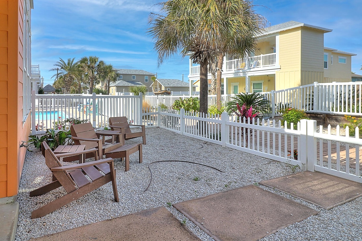 Relax in your private patio with comfortable seating, surrounded by tropical palms and colorful plants, overlooking the sparkling pool area.