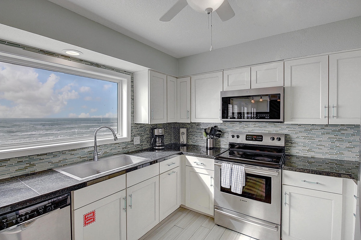Your fully equipped kitchen offers stunning ocean views while you cook, with modern appliances and sleek tile backsplash creating the perfect coastal cooking experience.