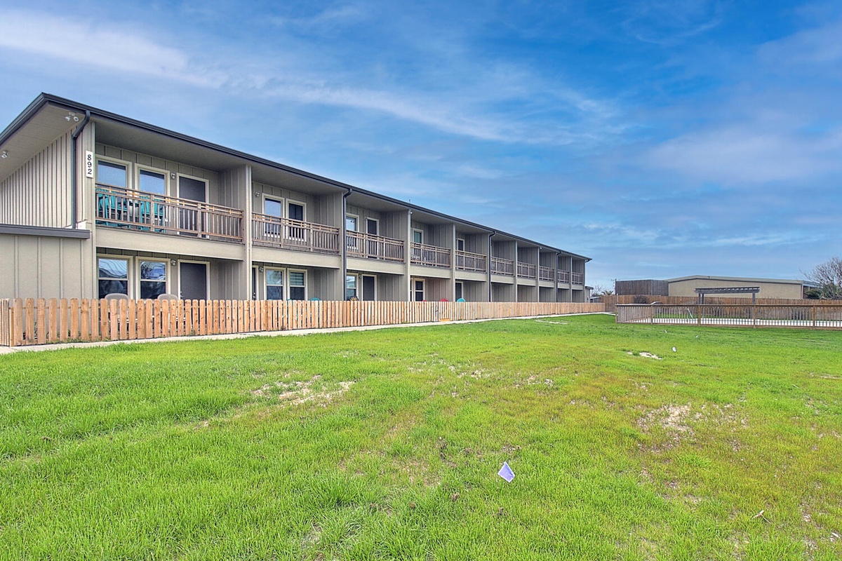 Multi-unit property building with individual balconies set on spacious green grounds under clear blue skies.