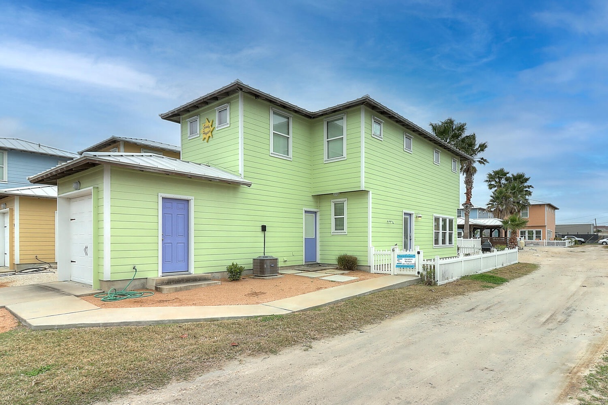 Bright green beach house with blue accents stands ready for coastal getaways in this charming beachside neighborhood.