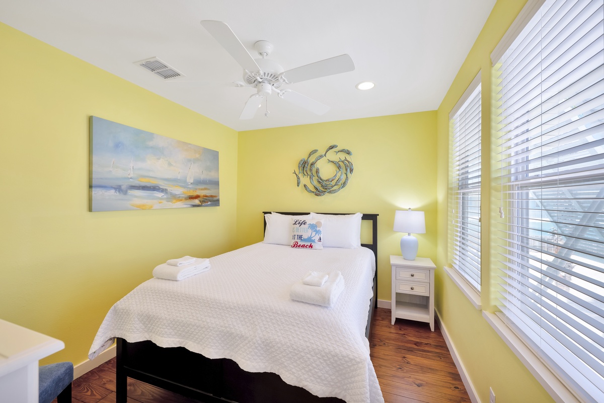 Drift off in your sunny bedroom with coastal artwork, comfortable bedding, and gentle ceiling fan breeze.