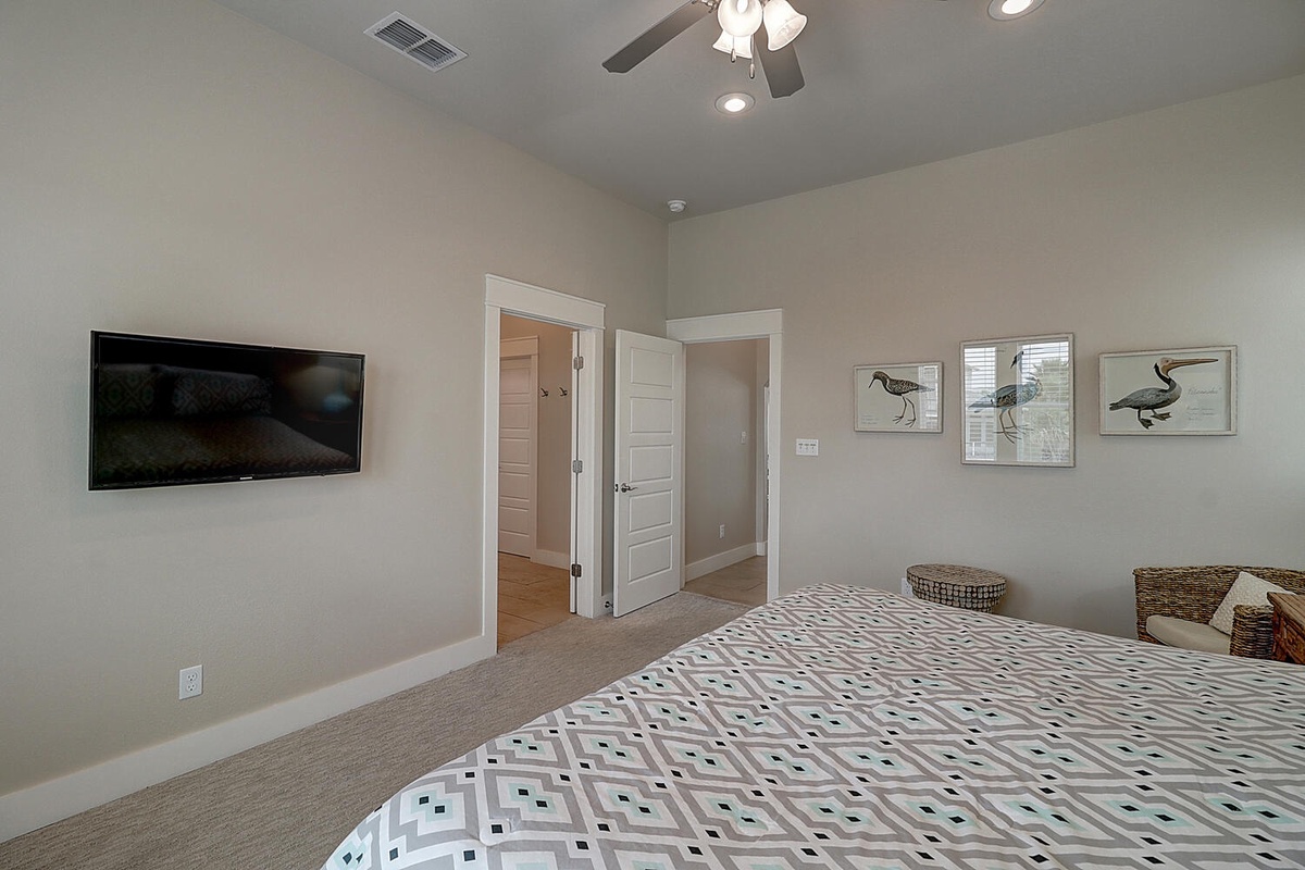 Relax in your peaceful bedroom with soft neutral tones, coastal artwork, and a wall-mounted TV for your evening entertainment.