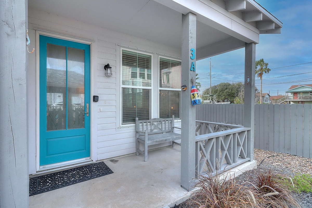 Charming coastal cottage entrance with bright turquoise door and covered porch in a quiet residential neighborhood.