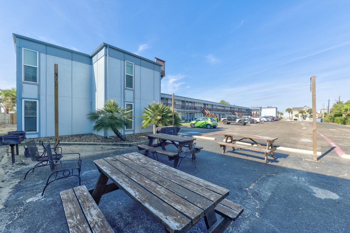 Modern motel property with outdoor picnic tables and palm trees under sunny blue skies.