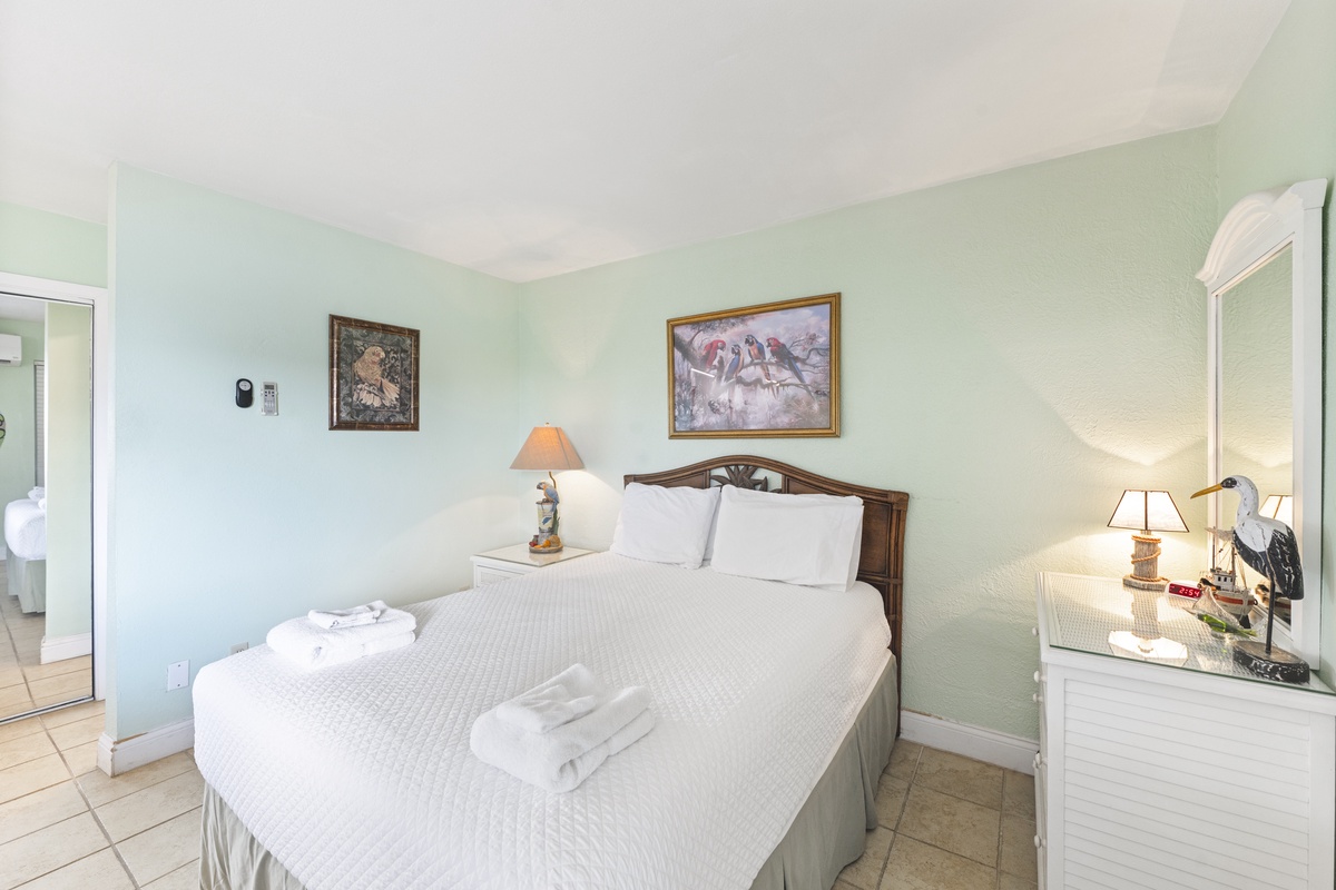 Relax in your serene bedroom with soft mint walls, crisp white linens, and charming bird artwork creating a peaceful coastal retreat.