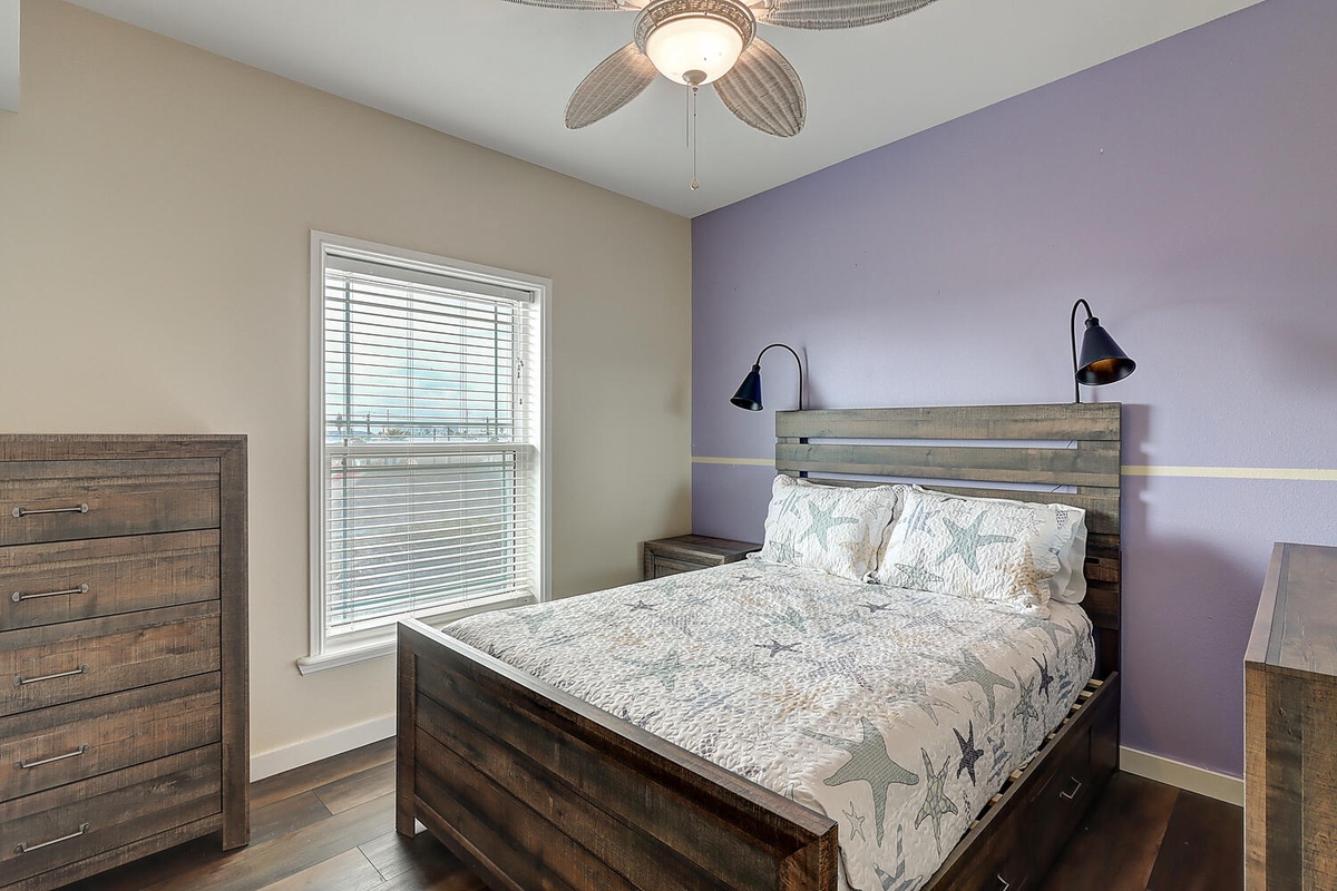Unwind in your tranquil bedroom featuring a plush queen bed, modern rustic furnishings, and soothing purple accent wall that creates the perfect retreat.