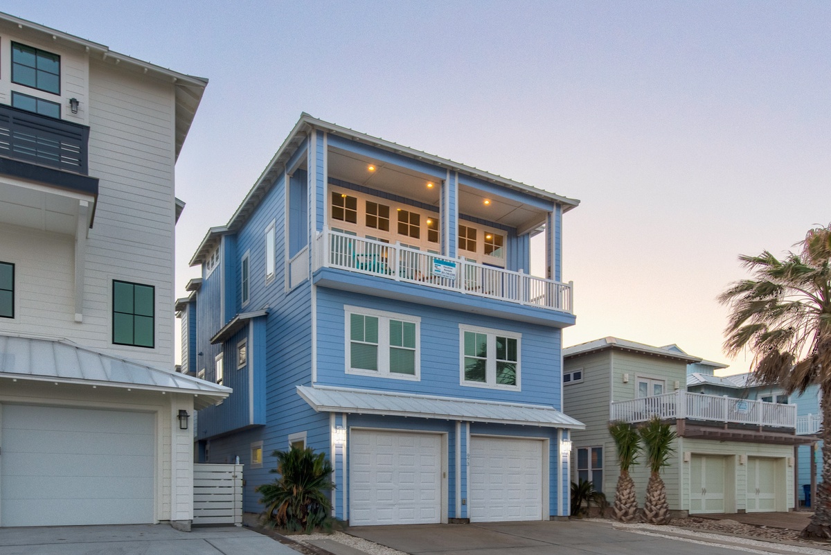 Charming blue beach house with covered balcony and garage space in coastal neighborhood.