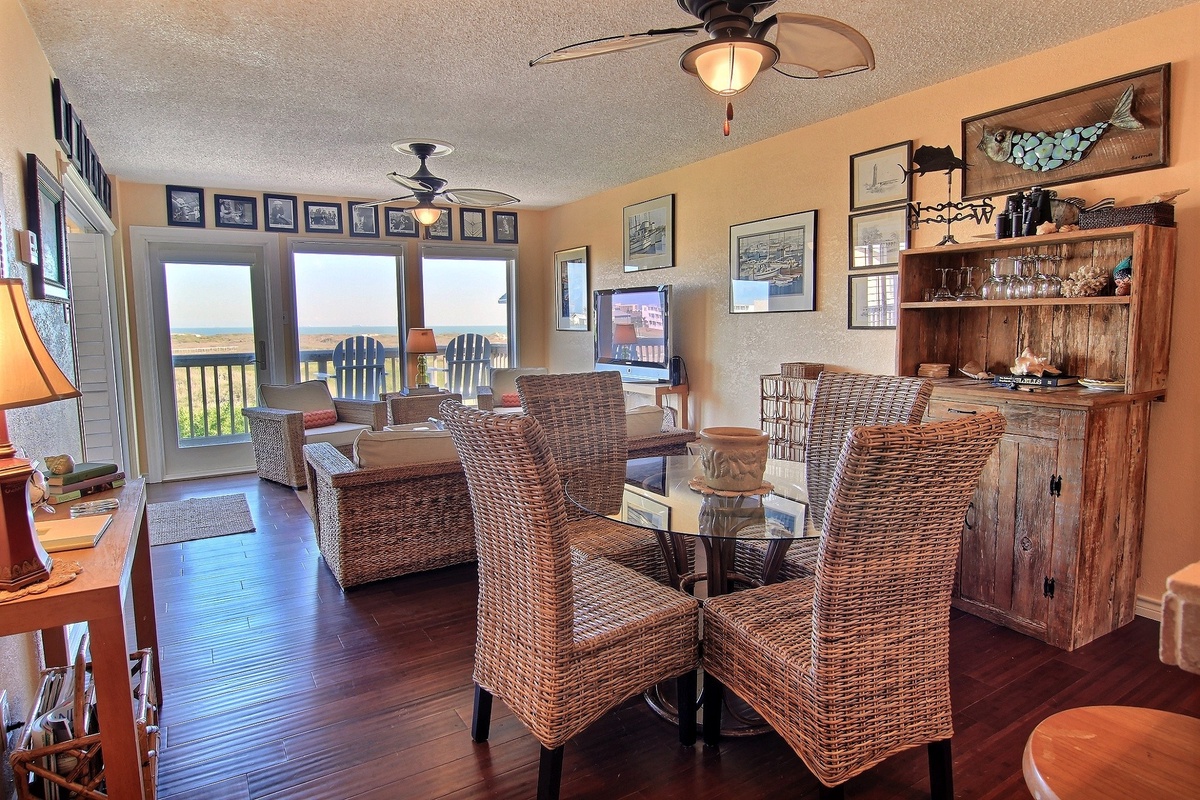 Your open living space flows seamlessly from cozy seating to the dining table, where warm wood tones create the perfect coastal retreat atmosphere.