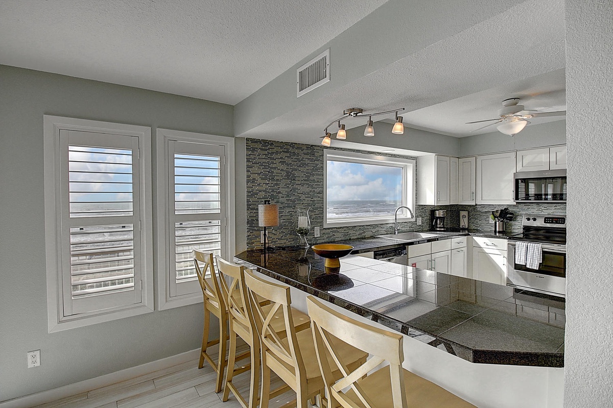 Your sleek kitchen features granite counters, modern appliances, and panoramic ocean views through plantation shutters - perfect for morning coffee.