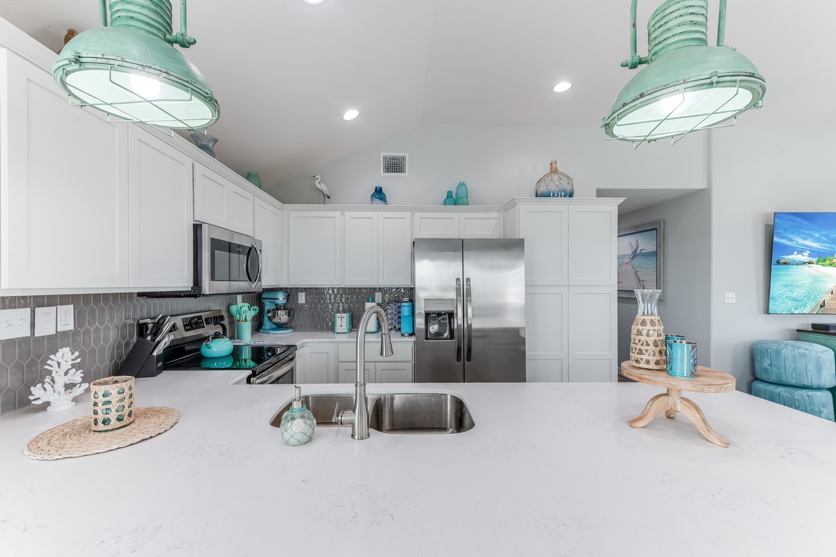 Your fully equipped kitchen awaits with coastal charm, featuring stainless steel appliances and serene turquoise accents perfect for preparing beachside meals.