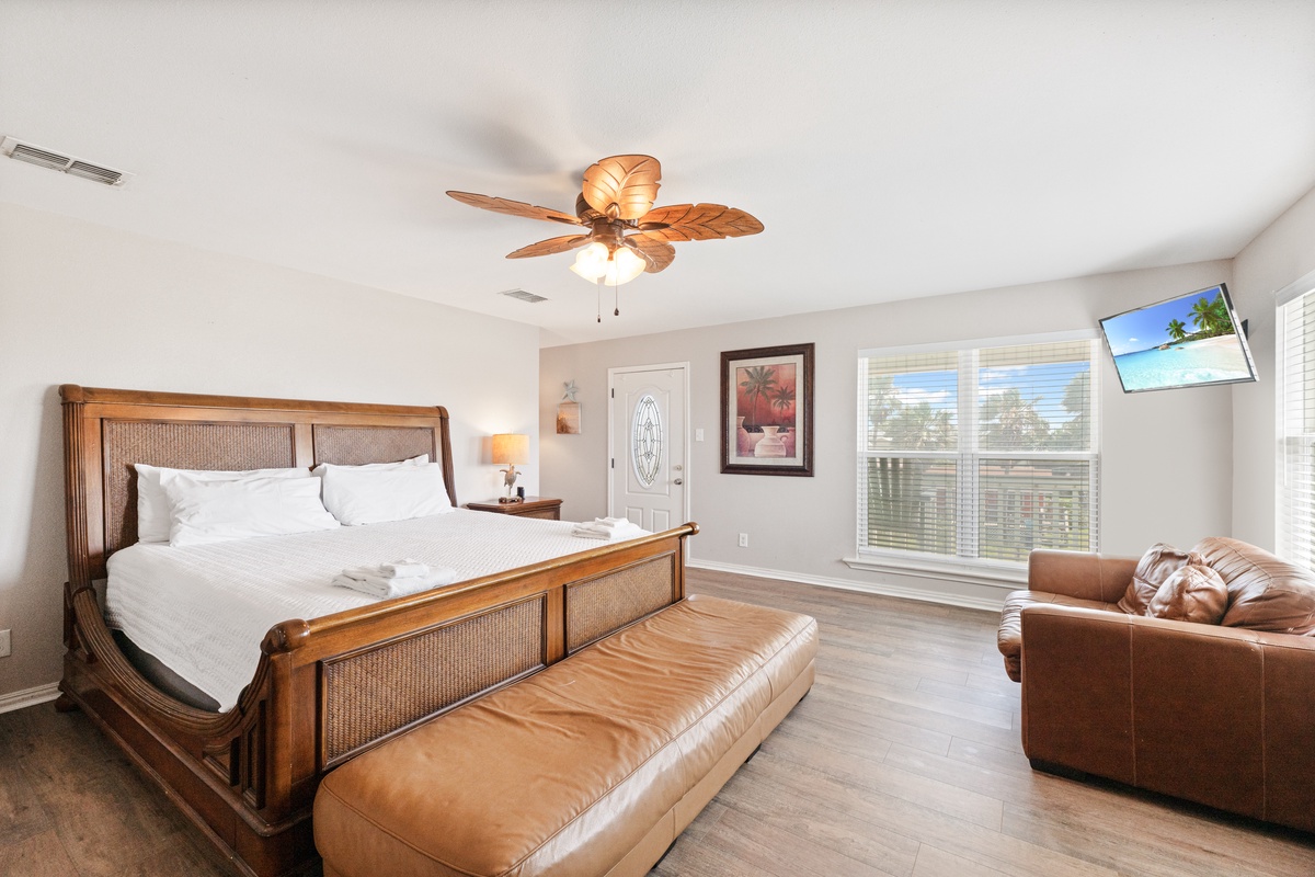 Unwind in your tropical-inspired bedroom with plush bedding, warm wood furnishings, and relaxing ceiling fan creating the perfect retreat atmosphere.