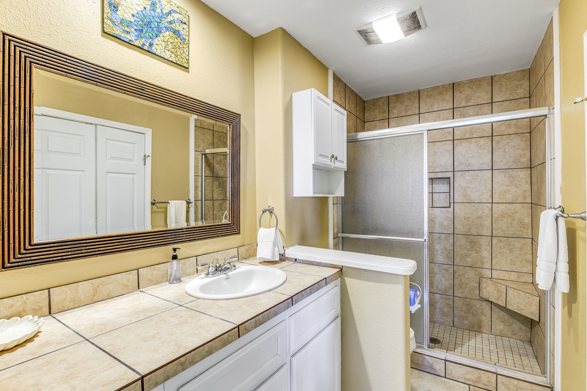 Unwind in your spacious bathroom featuring a tiled shower, vanity with storage, and thoughtful touches like fresh towels.