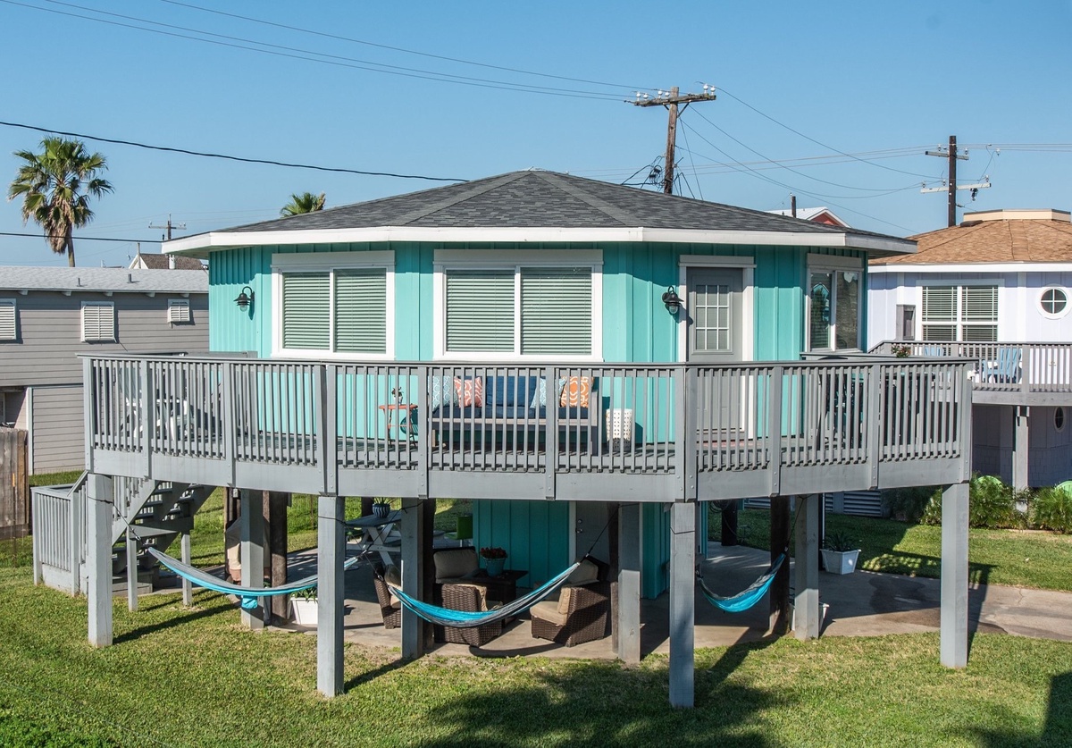 Charming beachside cottage on stilts with spacious wraparound deck and shaded hammock area below for ultimate relaxation.