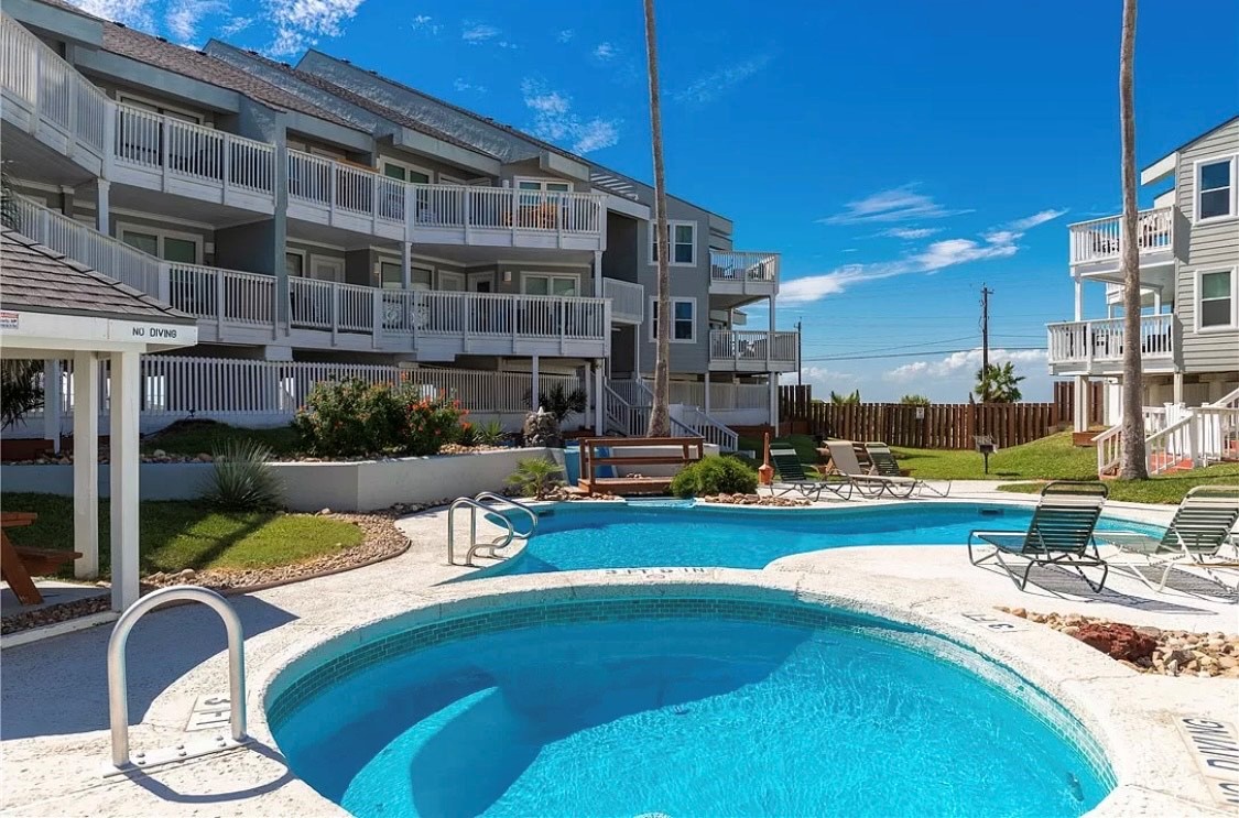 Stunning pool and hot tub await your relaxation, surrounded by comfortable lounge chairs and pristine coastal resort buildings.