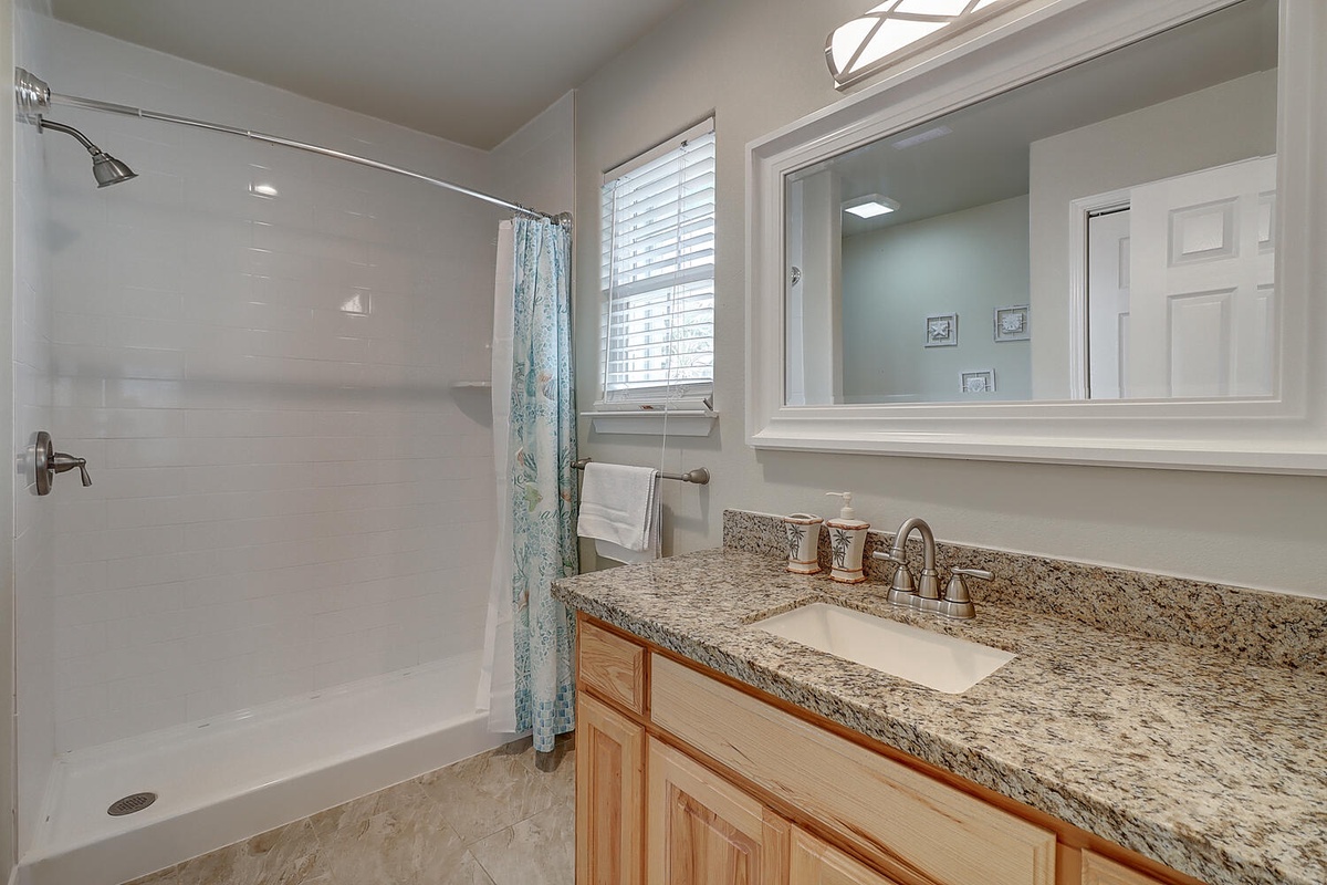 Refresh in your private bathroom featuring a granite vanity, spacious shower, and natural light streaming through the window.