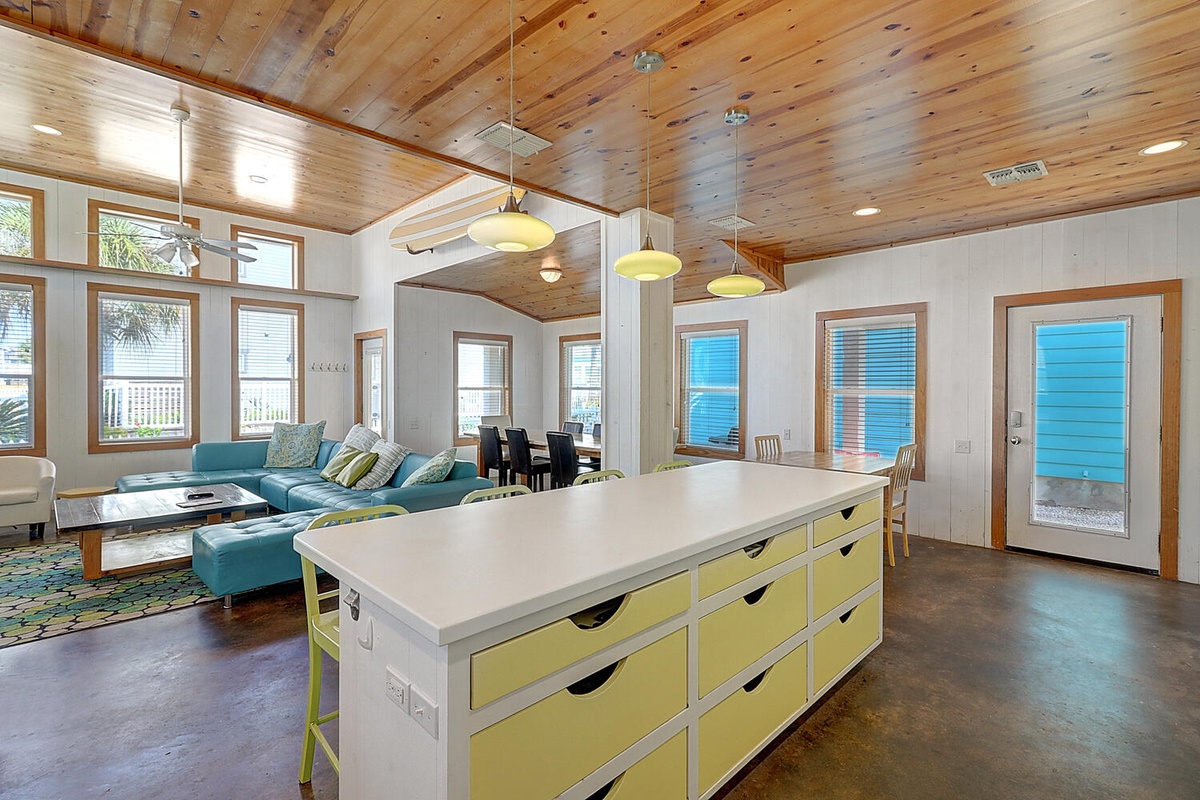 Your open-concept living space flows beautifully from kitchen to lounge, with warm wood ceilings and cheerful yellow accents creating a bright, welcoming atmosphere.