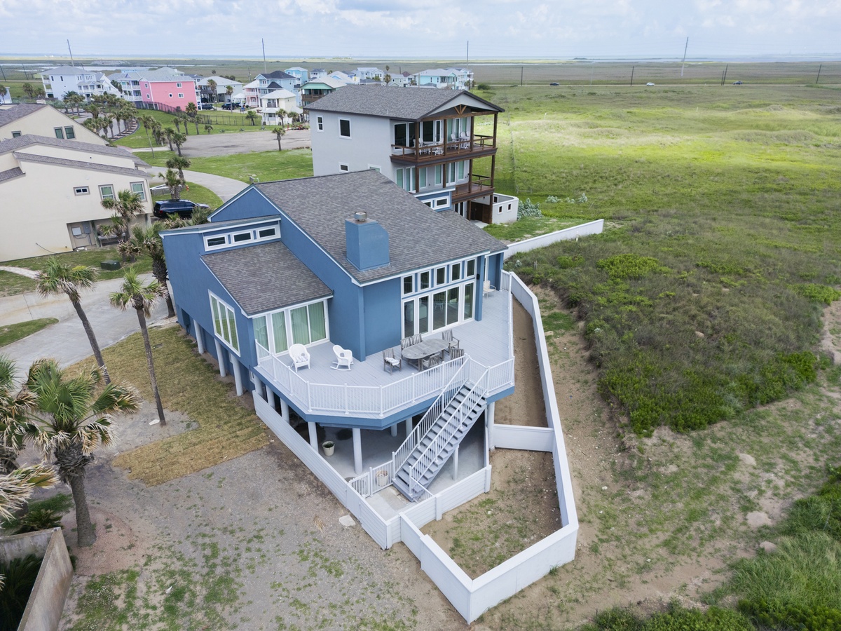 Coastal vacation home surrounded by natural marshlands, featuring elevated design and wraparound deck near neighboring beach properties.