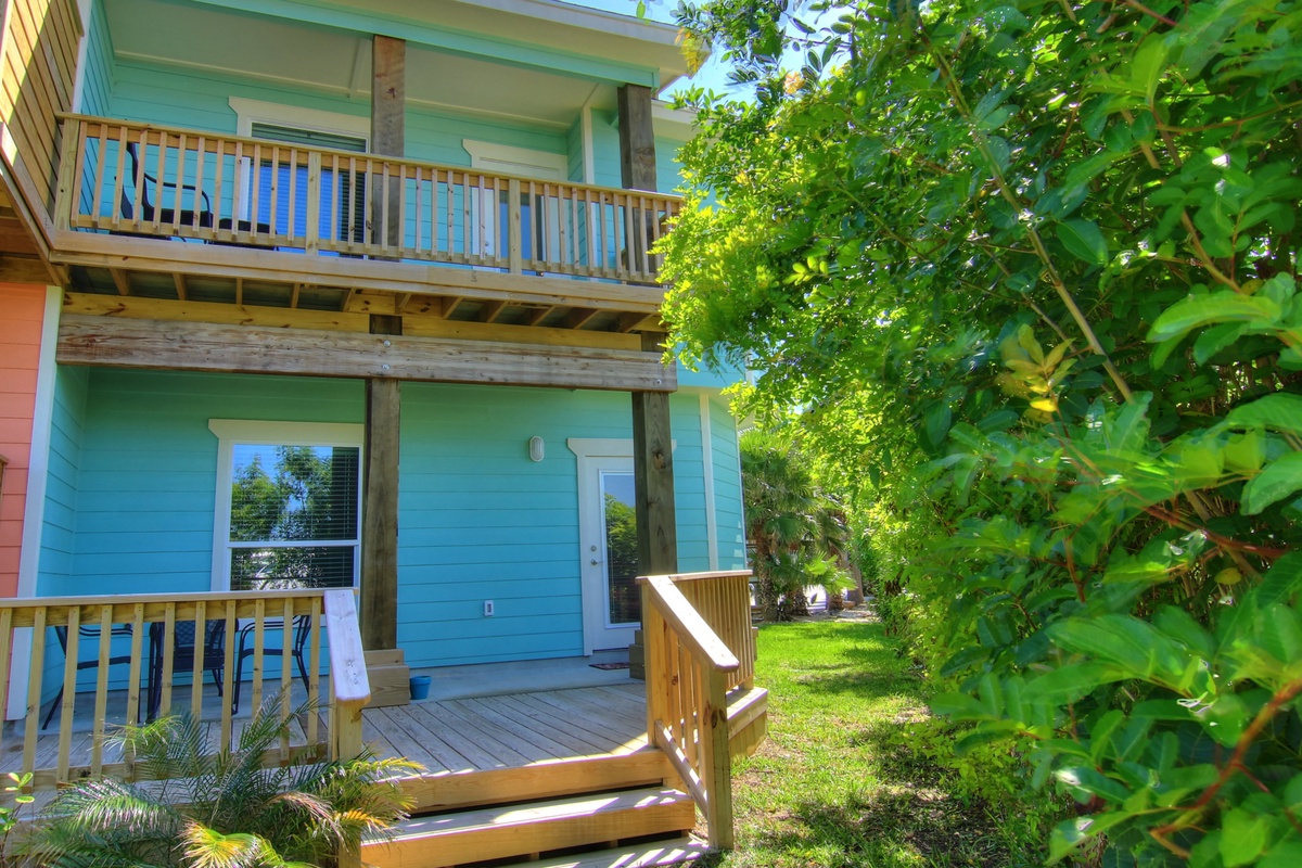 Colorful beachside building with wooden decks surrounded by lush tropical landscaping and mature shade trees.