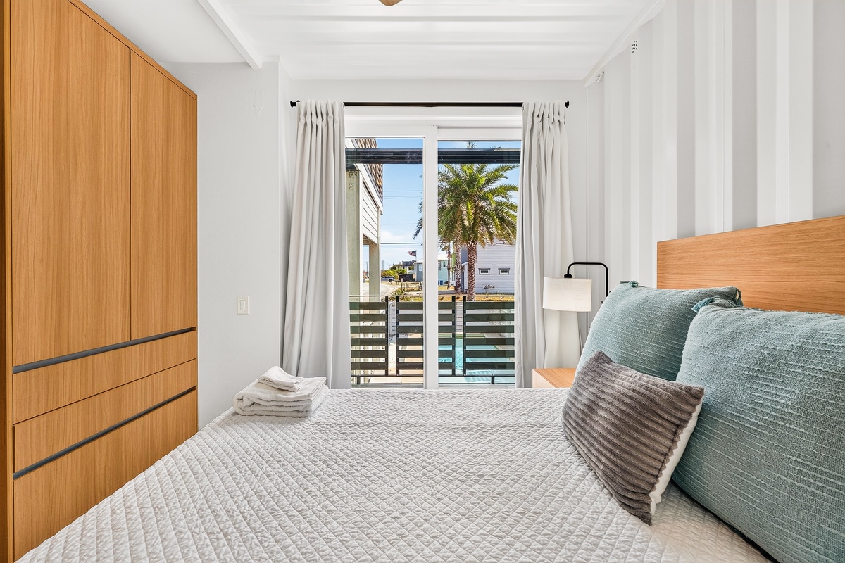 Slip into your serene third bedroom where crisp queen linens meet natural light. Step through the glass doors to your private balcony and feel the coastal breeze welcome you home.
