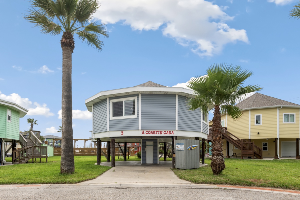 Charming coastal rental with palm trees and 'A Coastin Casa' signage welcomes guests to a tropical getaway.