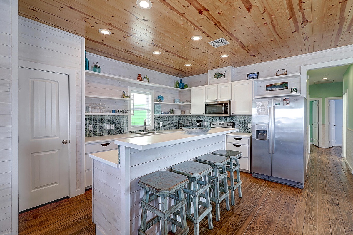 Your fully equipped kitchen features rustic wood ceilings, coastal tile backsplash, and a breakfast bar perfect for morning coffee.