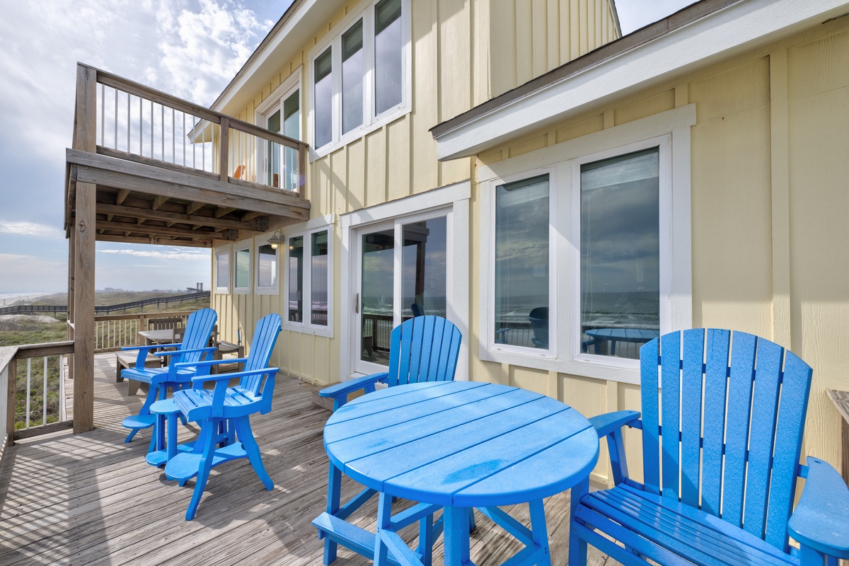 Relax on your private deck with vibrant blue Adirondack chairs and tables, perfect for morning coffee or evening conversations under the coastal sky.
