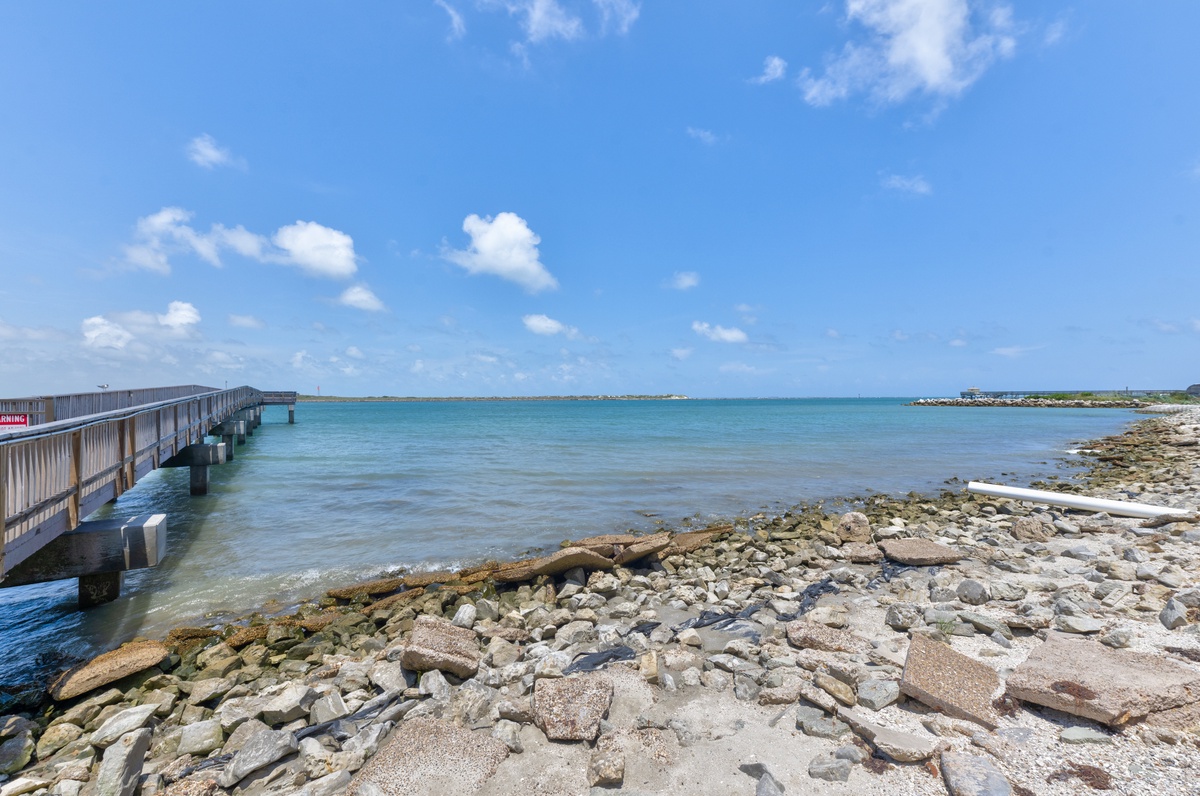 Stunning coastal views await with crystal-clear waters, rocky shoreline, and peaceful pier stretching into turquoise bay.