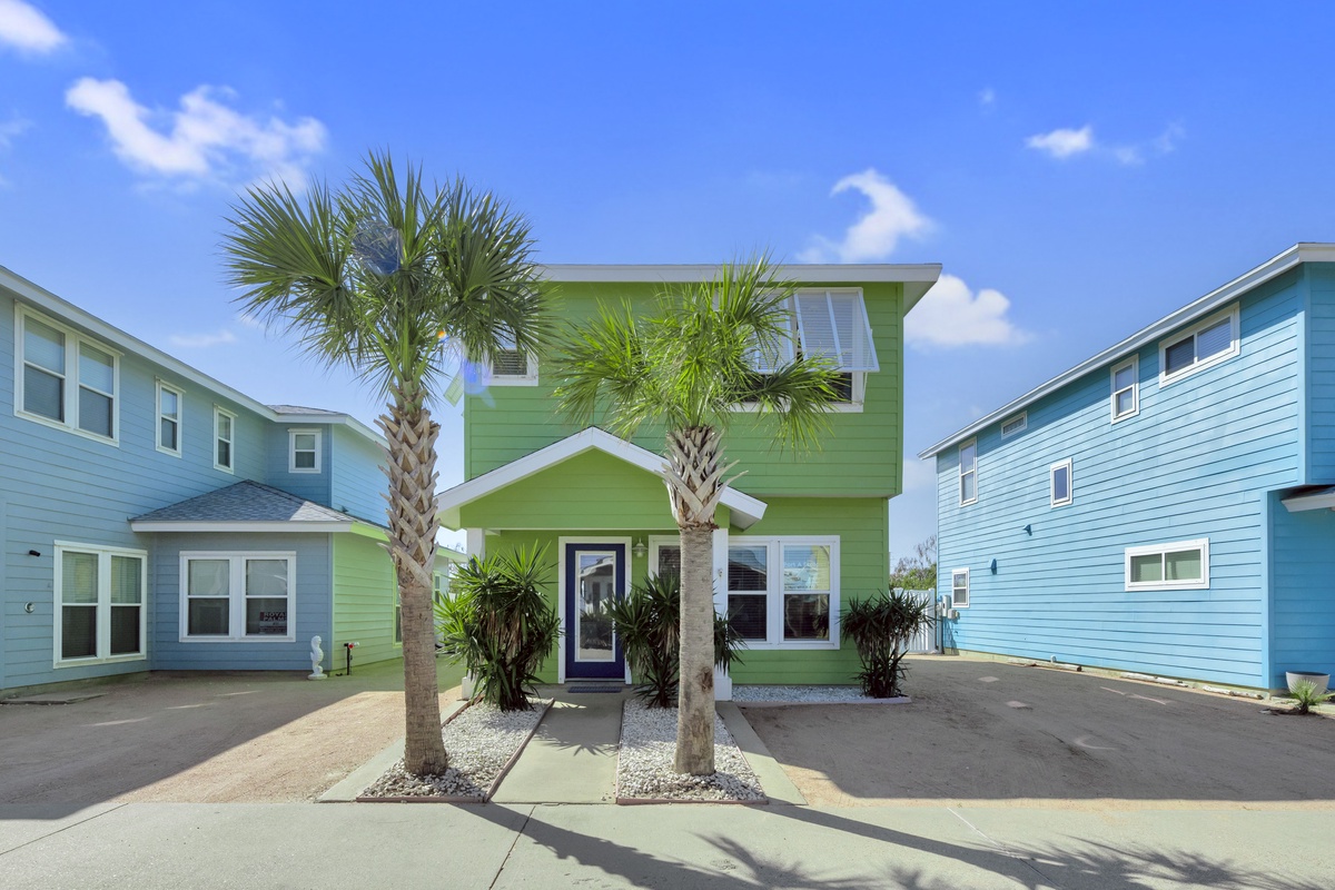 Vibrant coastal home with tropical palm trees and colorful neighborhood architecture under sunny blue skies.