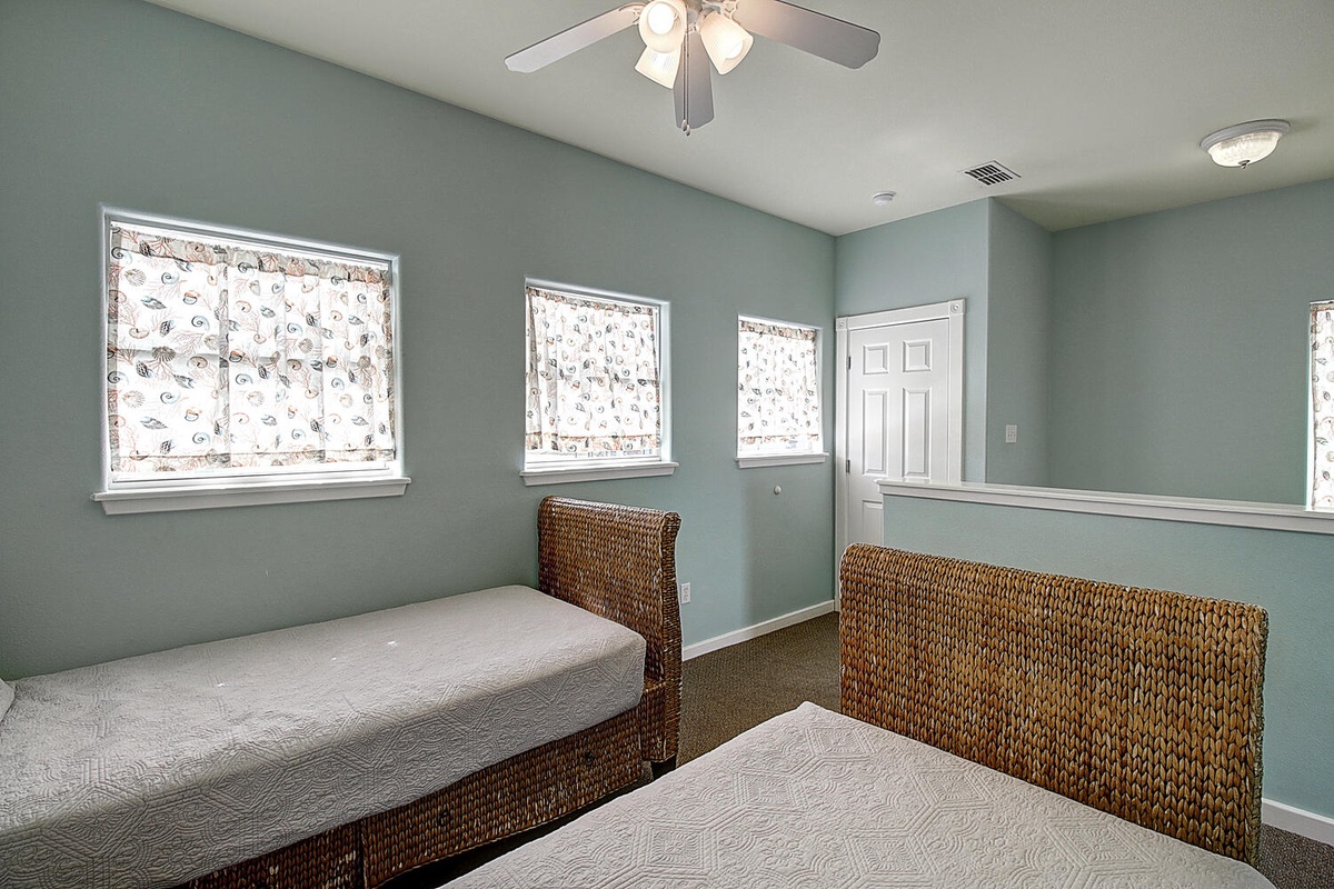 Settle into your peaceful twin bedroom featuring calming seafoam walls, charming nautical window shades, and natural wicker headboards.