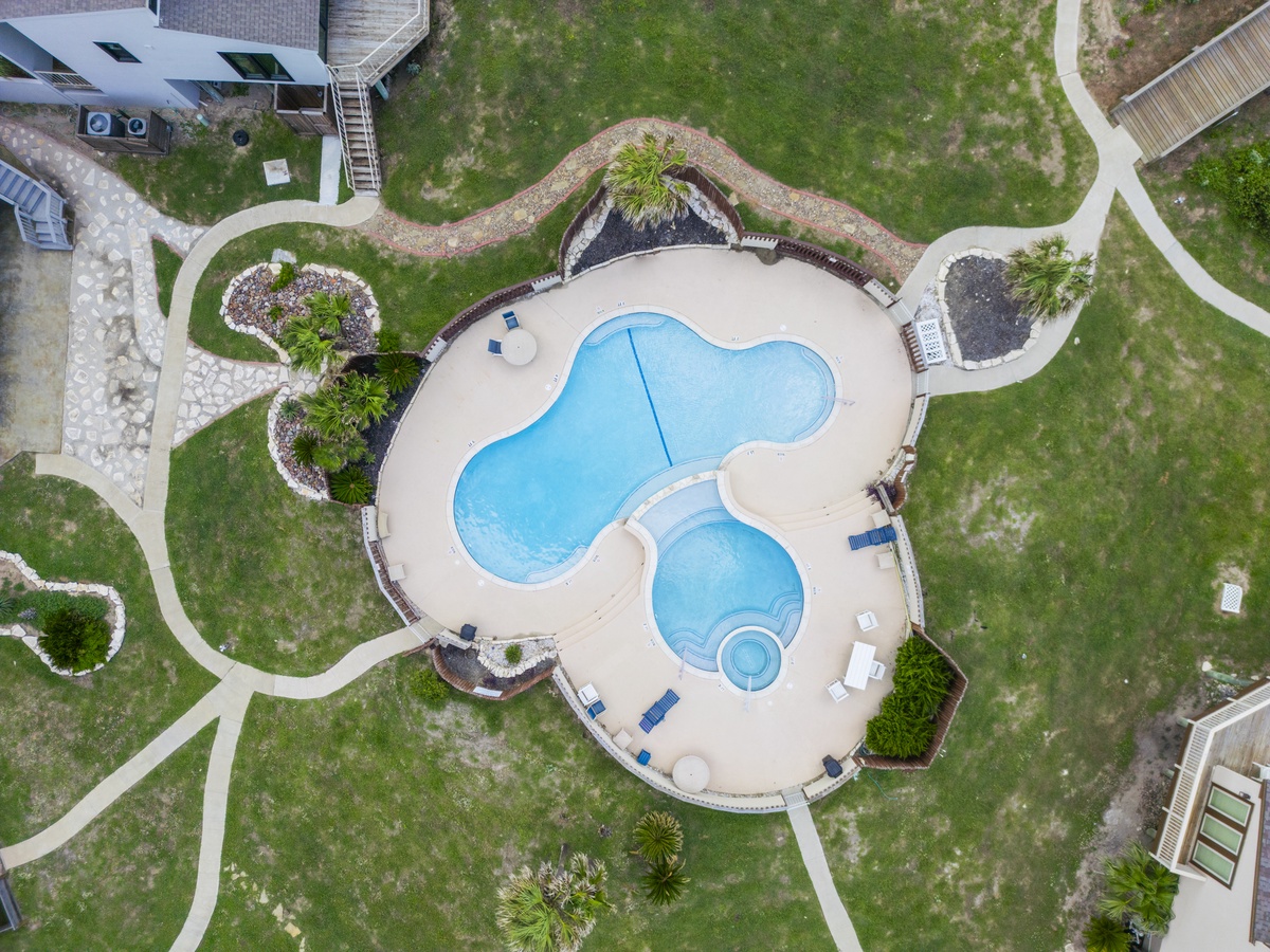 Aerial view reveals the property's distinctive free-form swimming pool with spa, surrounded by beautifully landscaped grounds and pathways.