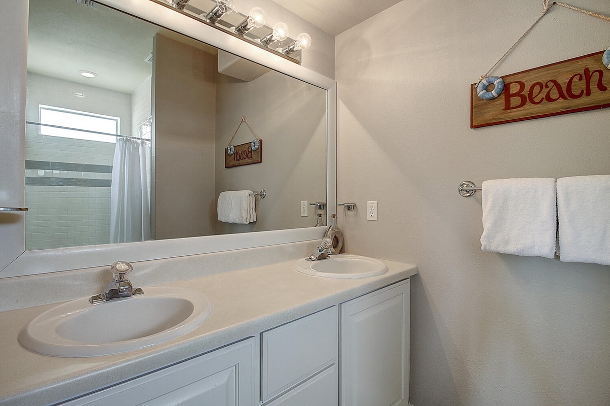 Step into your coastal-themed bathroom with dual sinks, bright vanity lighting, and charming beach décor that sets the perfect seaside mood.