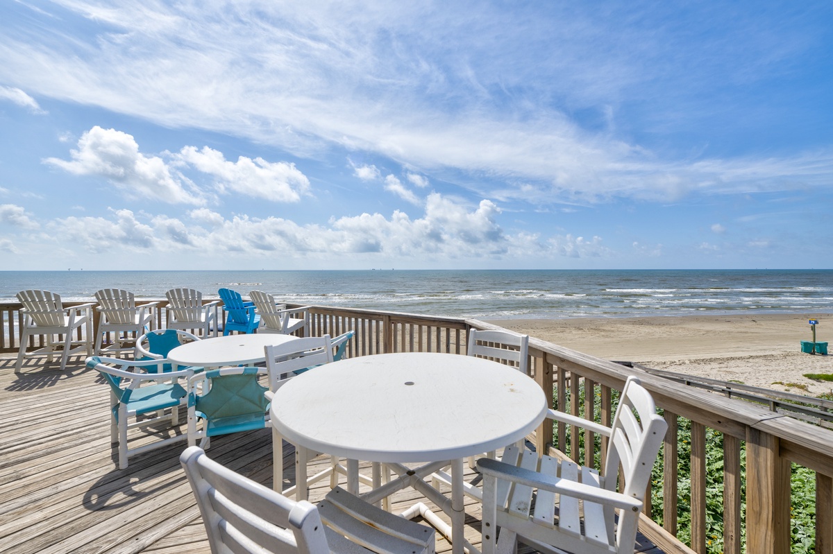 Expansive beachfront deck with panoramic ocean views, comfortable seating, and direct beach access under open coastal skies.
