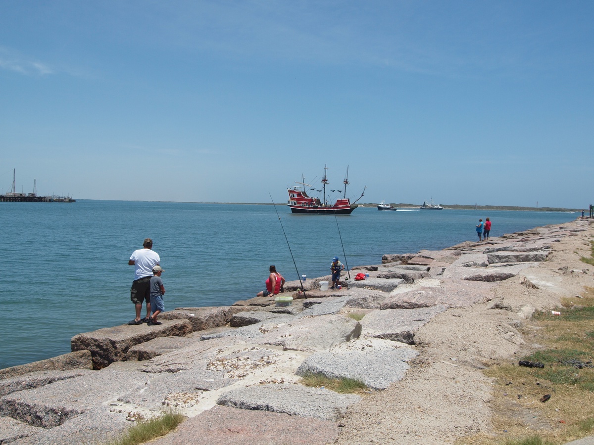 Coastal fishing spot with rocky shoreline where locals cast lines into calm blue waters beneath clear skies.